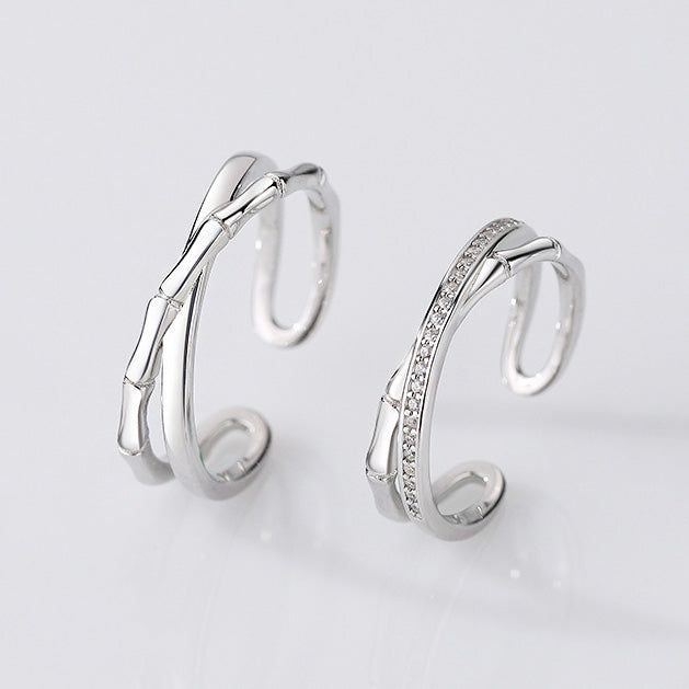 A pair of 925 sterling silver couple rings with a unique bamboo-cross design, one plain and one with stone embellishments.