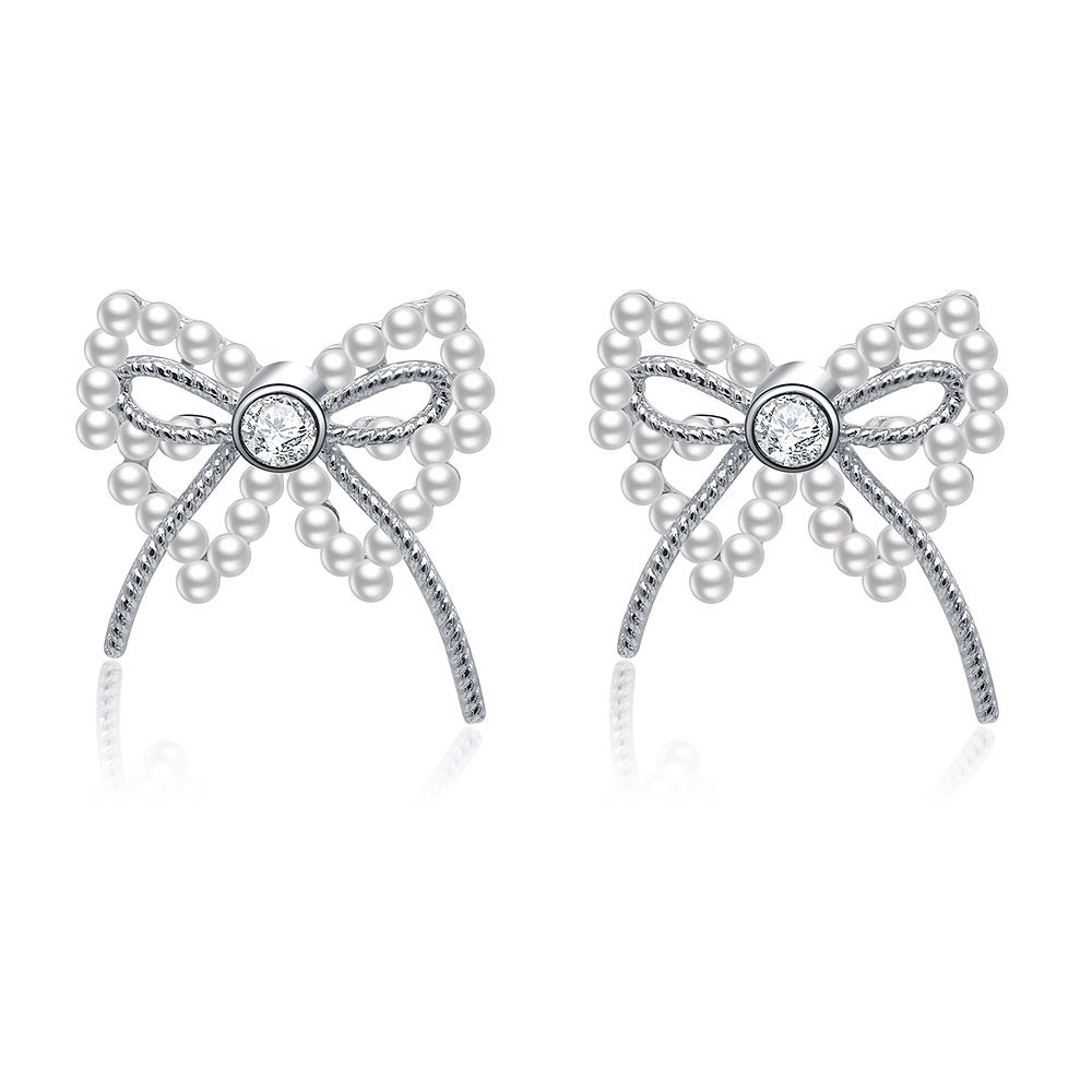 Une paire de boucles d'oreilles percées en forme de nœud en ruban de perles en laiton plaqué rhodium, mettant en valeur le design complexe du nœud avec une perle blanche centrale et des accents de zircon cubique étincelants.