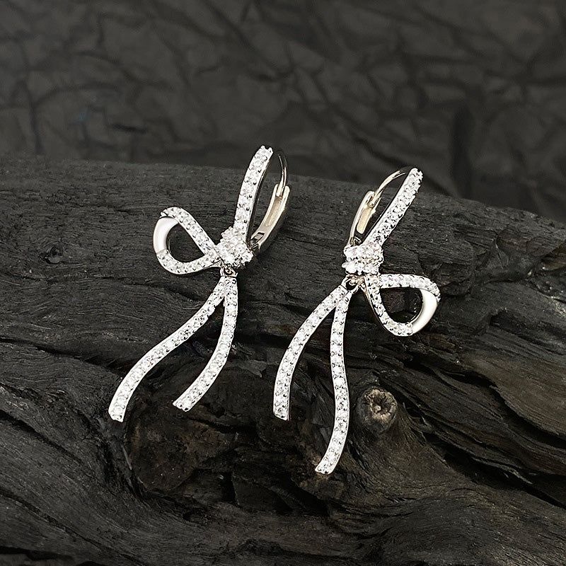 Un paio di orecchini a forma di fiocco dolce in argento sterling 925 con CZ, che mostrano il design intricato e le pietre bianche scintillanti su uno sfondo neutro.