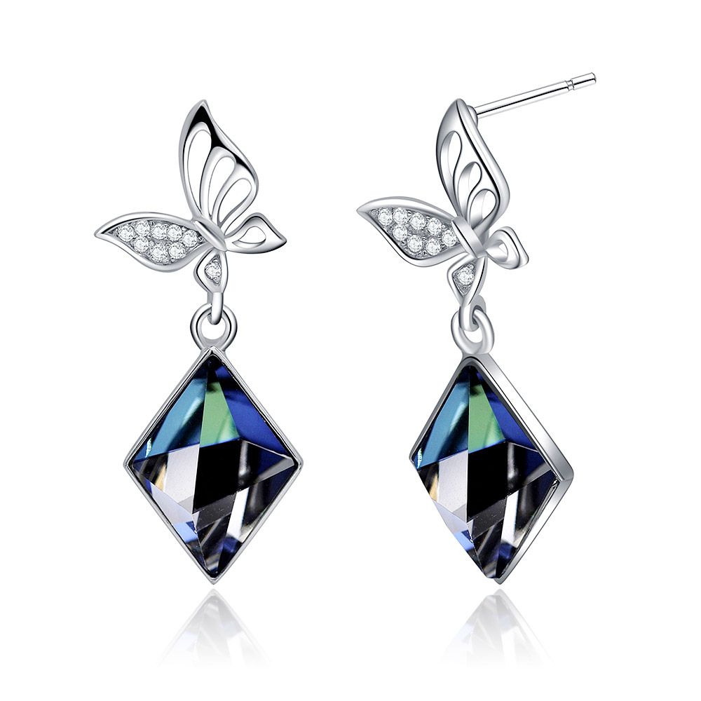 Gros plan sur des boucles d'oreilles pendantes en argent sterling 925 en forme de papillon, avec des ailes en pierre claire complexes et de grands cristaux Swarovski bleus facettés.