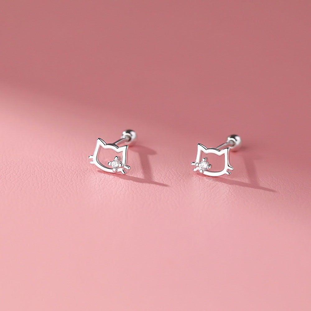 Une vue rapprochée des boucles d'oreilles en argent sterling en forme d'oreilles de chat, chacune présentant une pierre en zirconia cubique scintillante au centre, exposées sur une surface texturée.