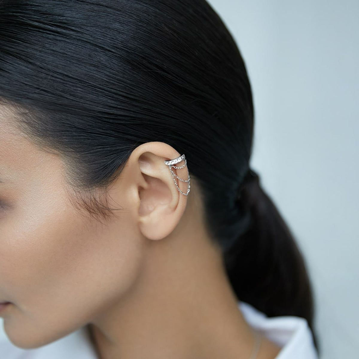 Uma visão de perto de uma mulher usando o brinco de corrente CZ em prata esterlina 925, destacando seu design ajustável e sem furo, e estilo minimalista.