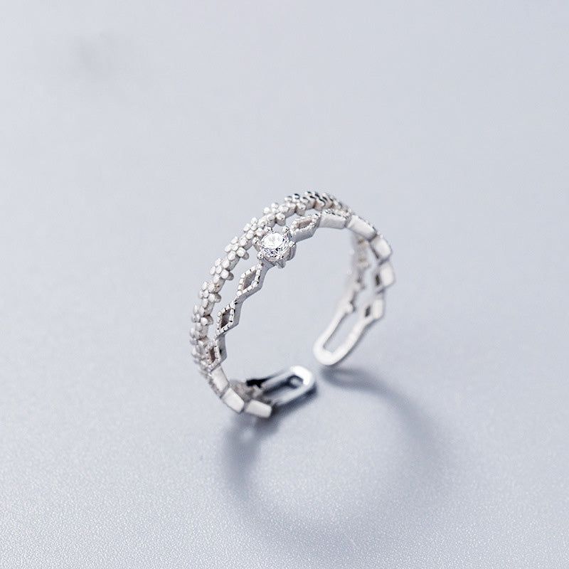 Un primer plano de un anillo ajustable de plata esterlina S925 con un intrincado diseño de encaje de flores y una piedra central de circonio cúbico.