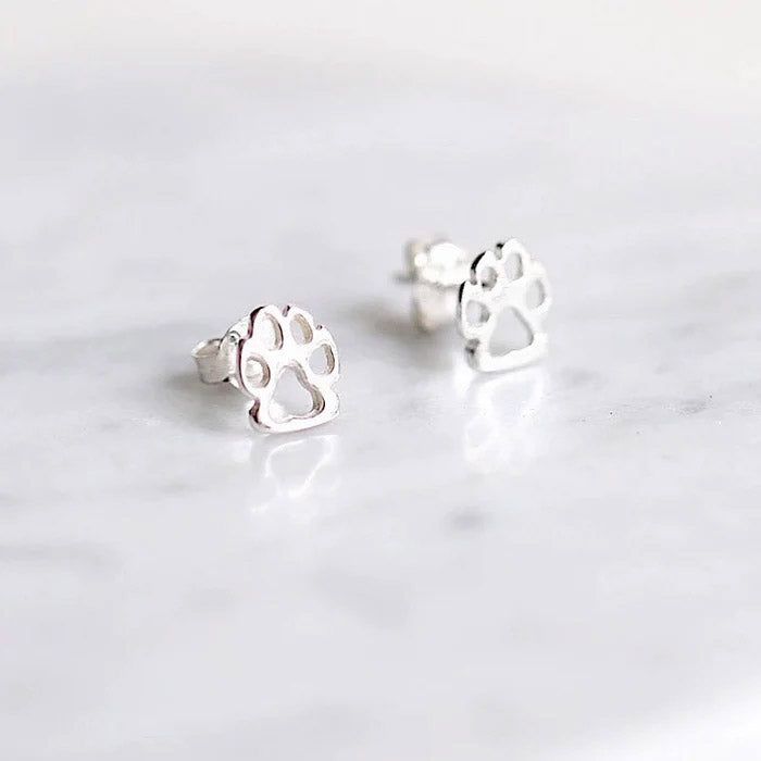 Un paio di orecchini a perno in argento sterling 925 a forma di impronte di zampe di cane, esposti su una superficie di marmo bianco.