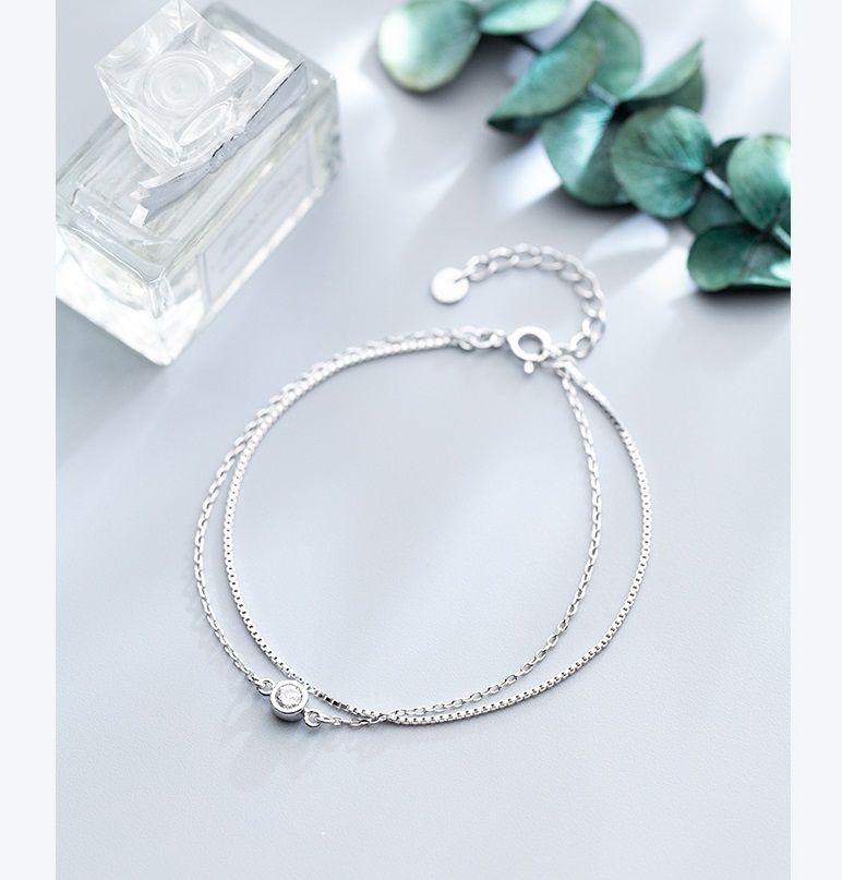 Un primo piano del bracciale solitario con doppia catena in argento sterling 925, che mostra i suoi delicati doppi fili e il ciondolo centrale incastonato su uno sfondo bianco.