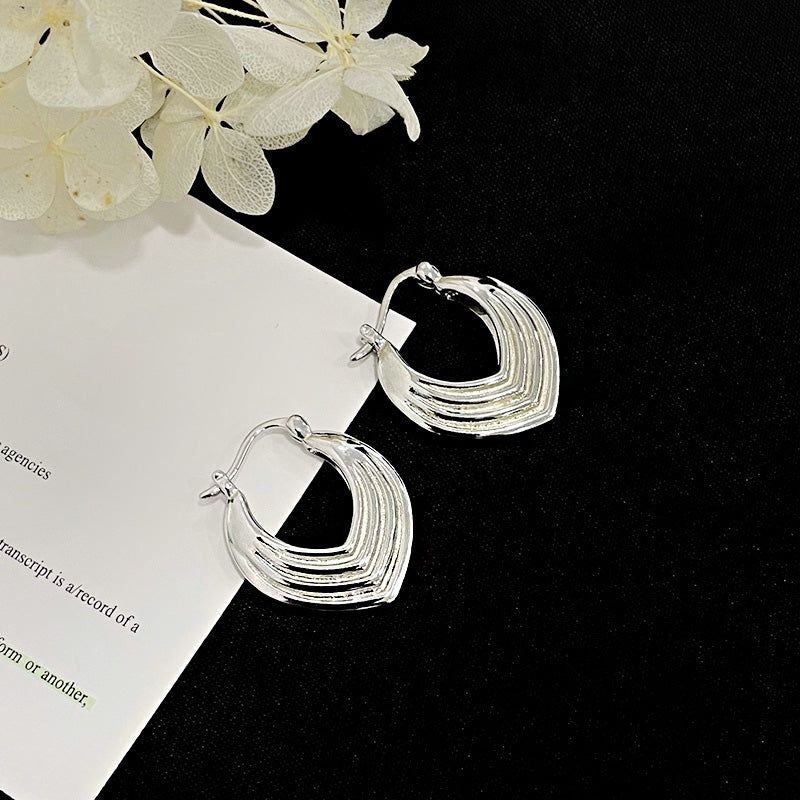 Un paio di orecchini a cerchio geometrici a scudo stratificato in argento sterling 925 su uno sfondo bianco pulito, che mostrano il loro design intricato.