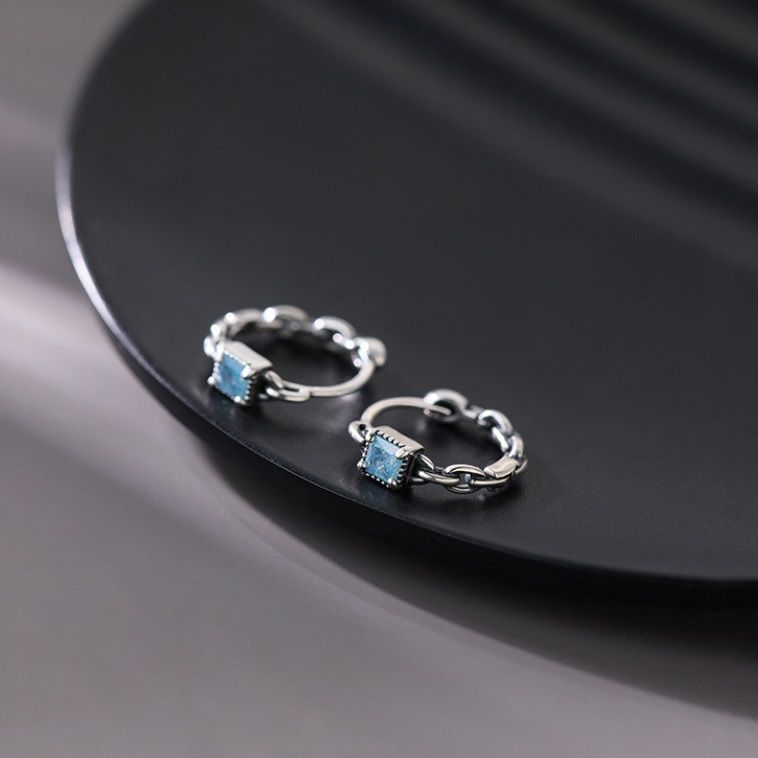 Un paio di orecchini a perno geometrici a cubo di menta in argento sterling 925 con gemme di zirconia cubica blu scintillanti su uno sfondo bianco.