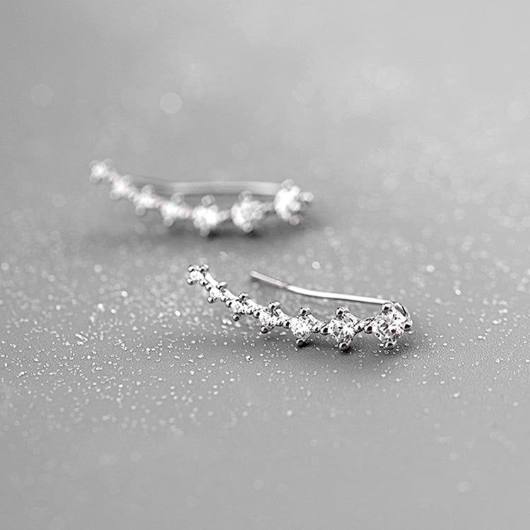 Un paio di orecchini a perno a climber in argento sterling 925 con sette zirconi scintillanti, elegantemente curvati e esposti su uno sfondo neutro.