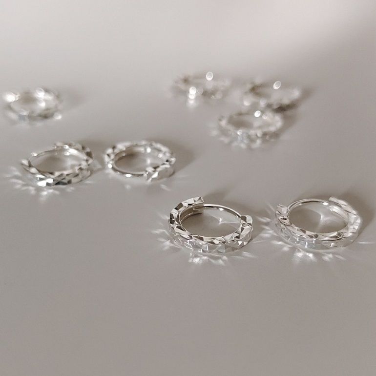 Un paio di orecchini a gancio in argento sterling 925 con taglio a diamante che mostrano la loro intricata texture sfaccettata su uno sfondo bianco.