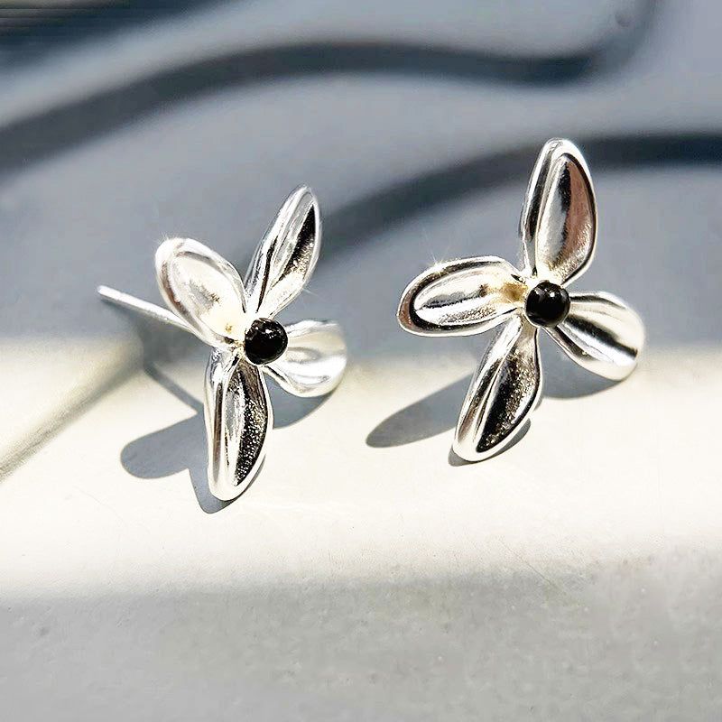 Un primo piano di un paio di orecchini a bottone a forma di fiore in argento sterling 925 con centri in onice nero lucido, su uno sfondo bianco pulito.