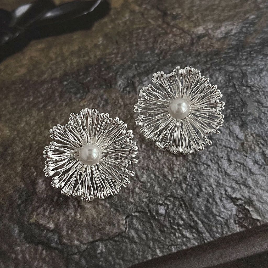 Une paire de boucles d'oreilles florales affirmées en laiton argenté, chacune présentant un design de pétale complexe avec une perle brillante au centre.