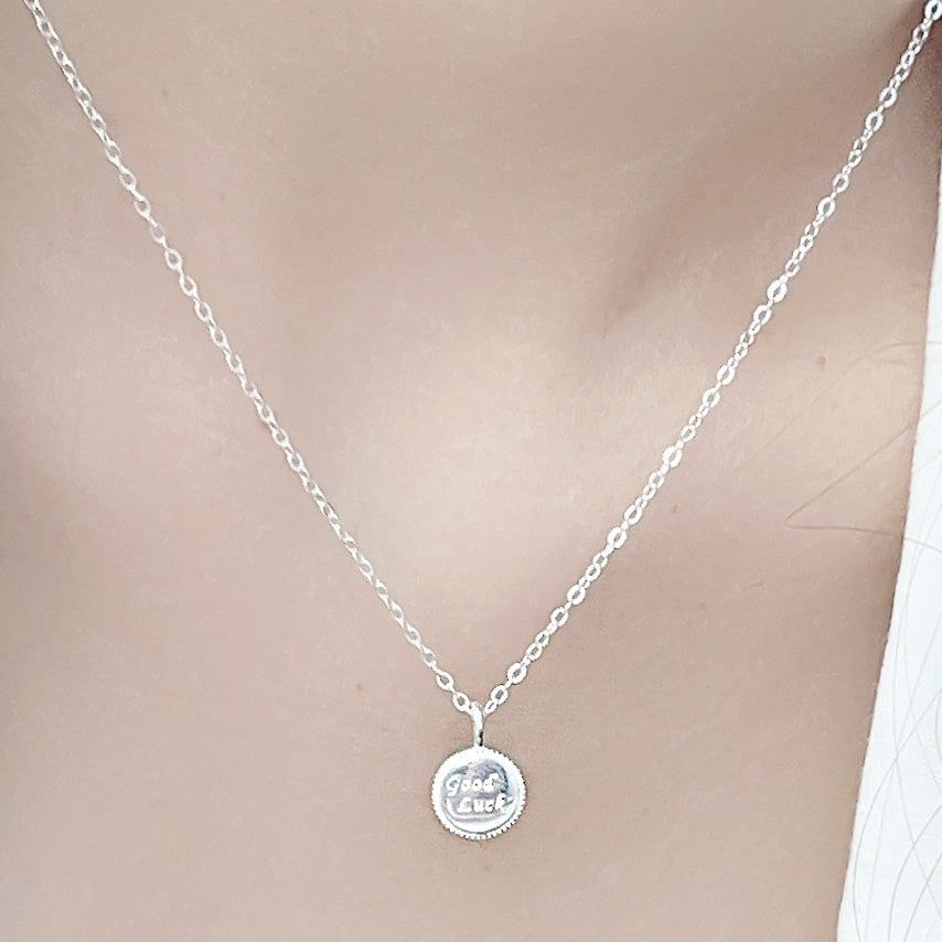 Un gros plan en studio d'un collier en argent sterling 925 avec un pendentif en forme de pièce 'Bonne Chance', sur un fond blanc propre.