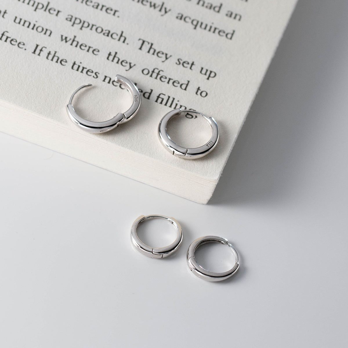 Un set di cinque orecchini a cerchio minimalisti in argento sterling 925 con una finitura opaca, esposti su uno sfondo pulito e chiaro.