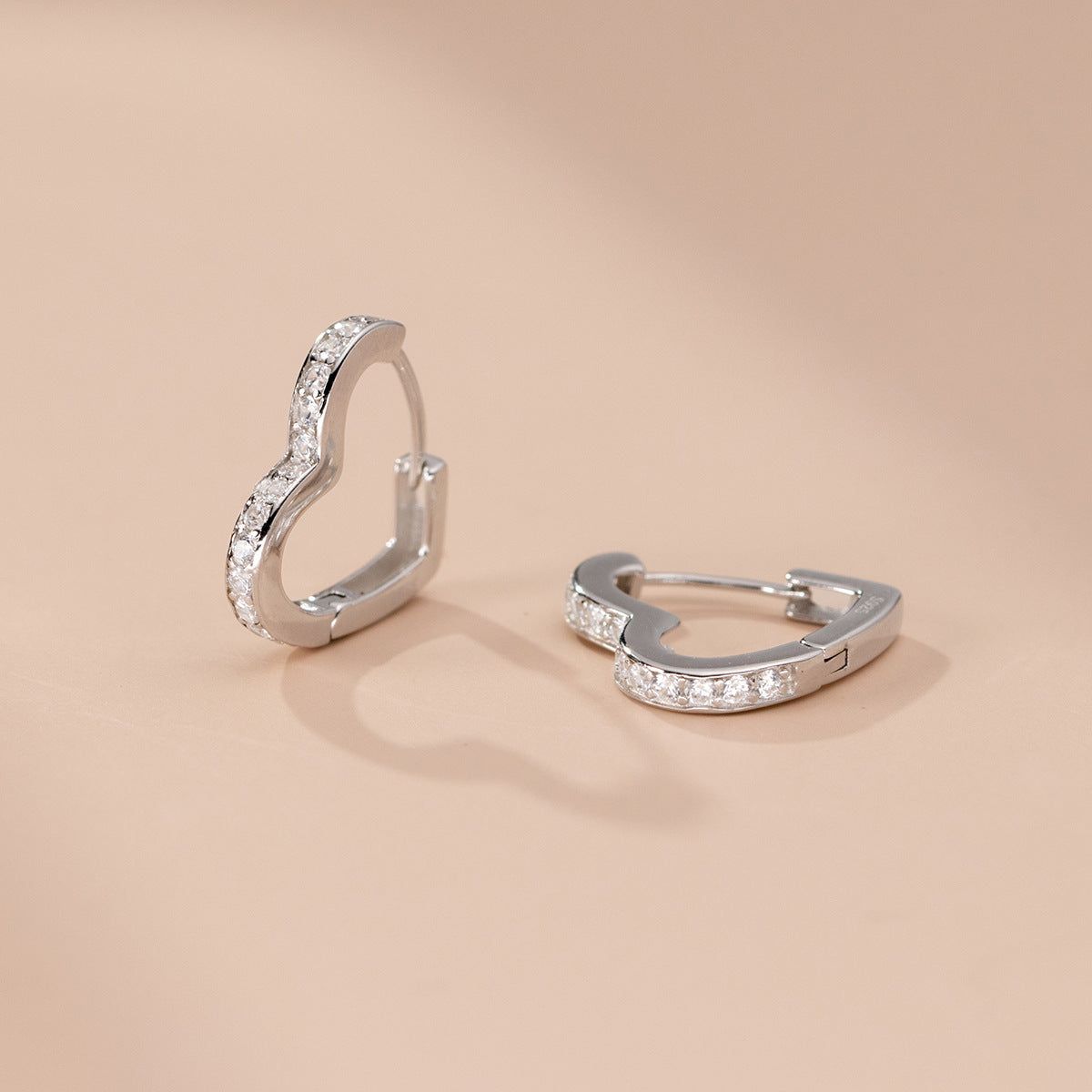 Un paio di orecchini a cerchio a forma di cuore in argento sterling 925, elegantemente accentuati da scintillanti pietre di zirconia cubica, esposti su uno sfondo bianco.
