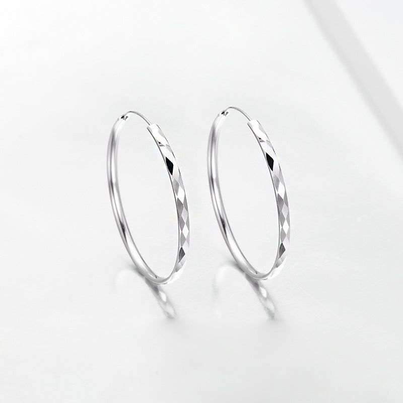 Una foto ravvicinata del prodotto degli orecchini a cerchio in argento sterling 925, con una texture a taglio diamante dettagliata e una finitura lucida.