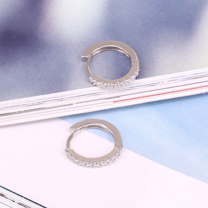 Primo piano di un paio di orecchini a cerchio in argento sterling 925, elegantemente dettagliati con pietre di zirconia micro-inserite, su uno sfondo neutro.