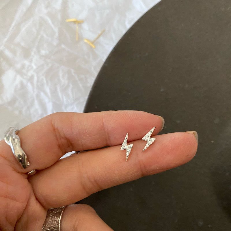 Una vista ravvicinata di un paio di orecchini a perno a forma di fulmine in argento sterling 925, incastonati con zirconia scintillante, tenuti tra due dita.