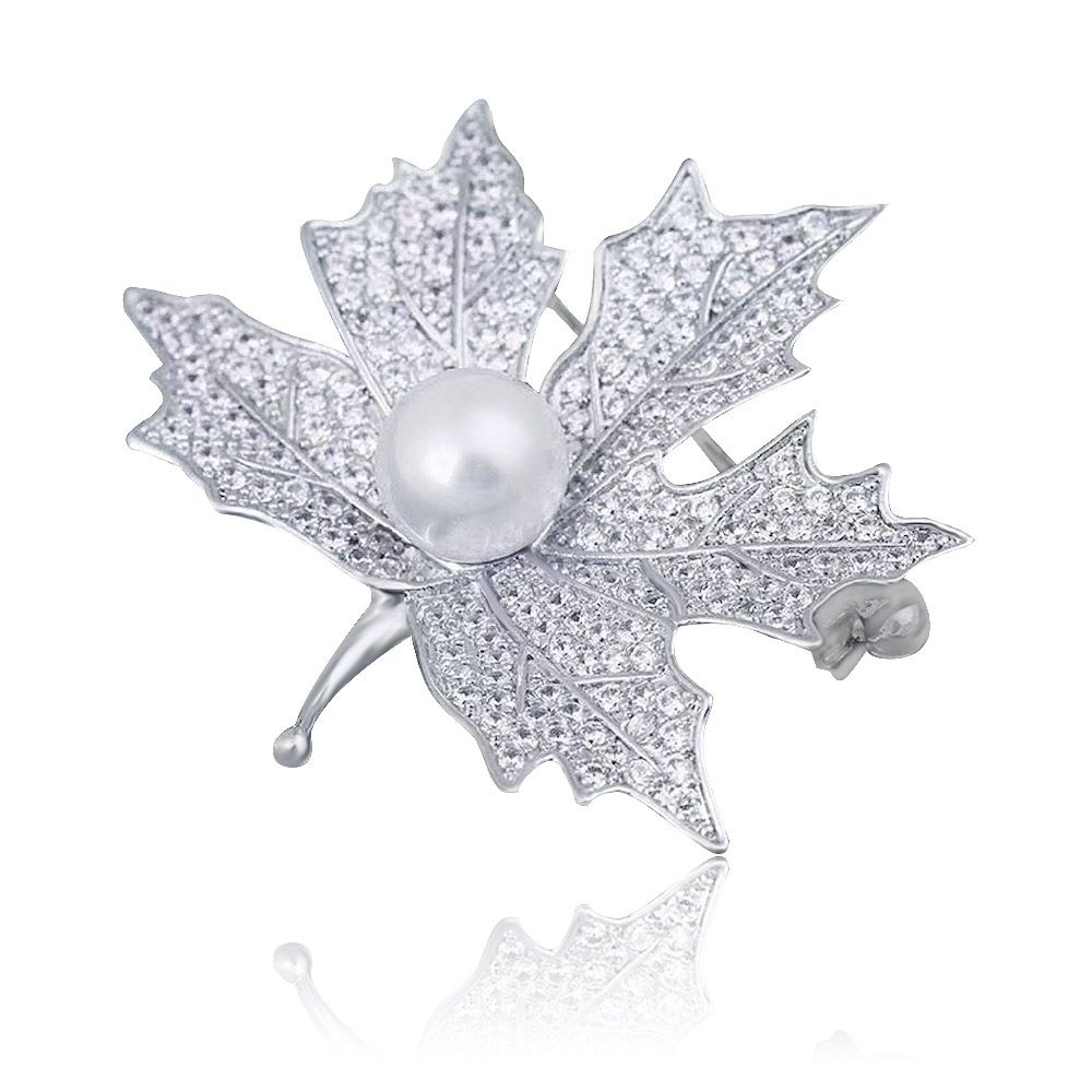 Primer plano del broche de hoja de arce delicada, mostrando su intrincado diseño en plata con una perla blanca central y piedras de circonio cúbico brillantes sobre un fondo blanco.