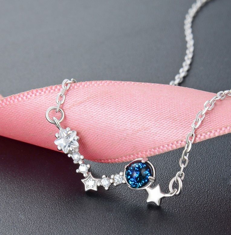 A detailed studio shot of the 925 Sterling Silver Wishing Stars Necklace, highlighting its central blue gemstone and delicate star-shaped cubic zirconia charms on a silver chain.