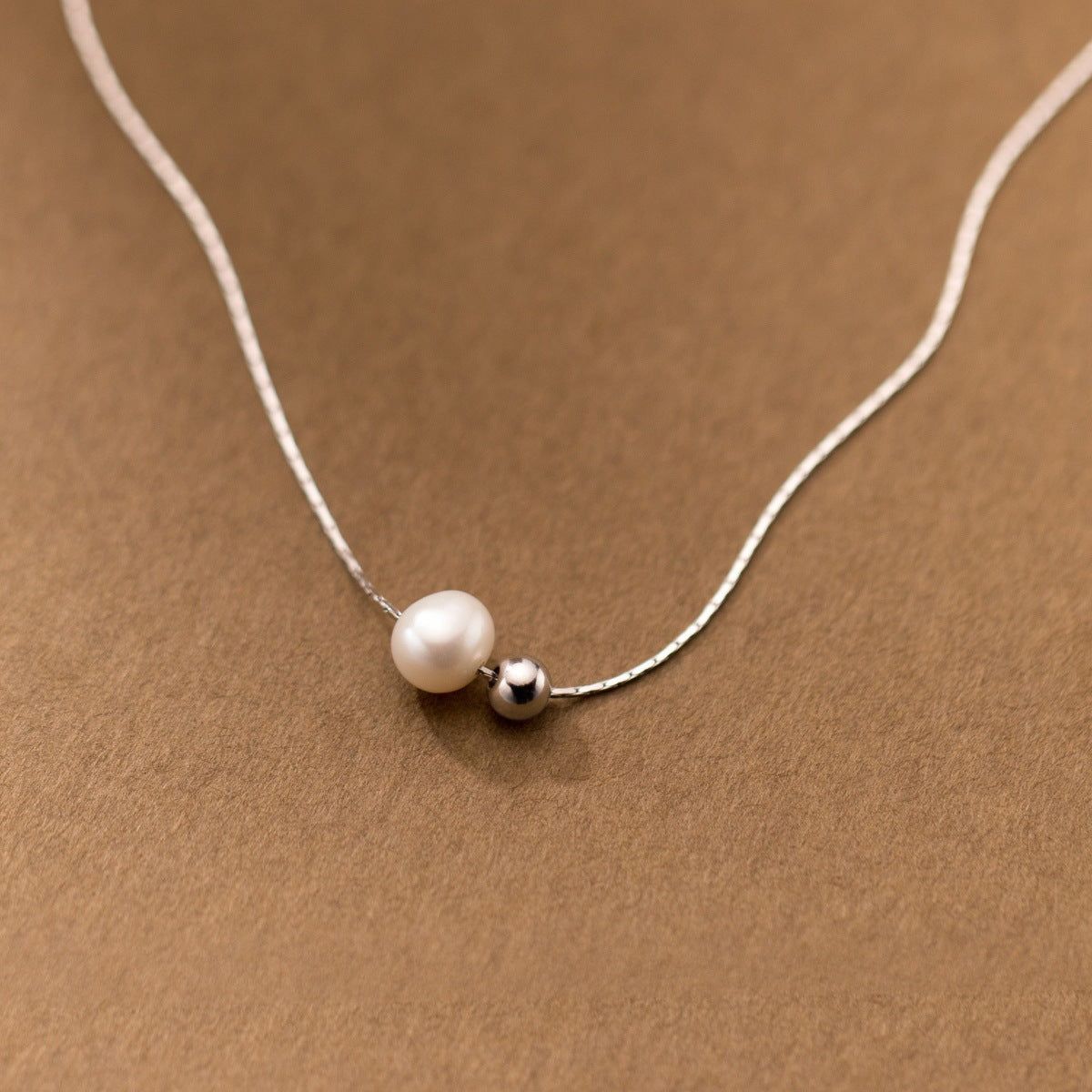 A close-up product shot of a 925 sterling silver snake chain necklace featuring a single elegant white pearl and a small silver bead.