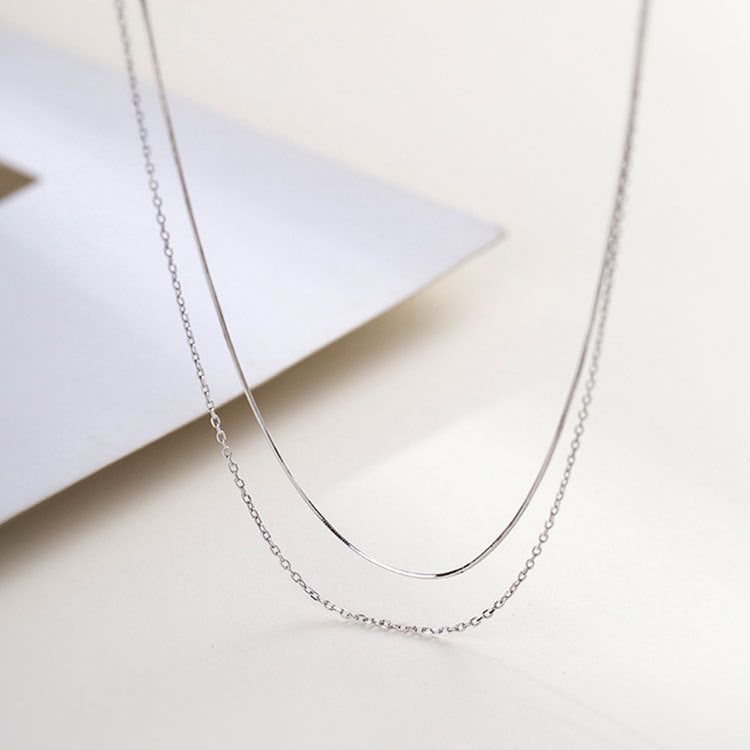 Un set di collane a doppio strato in argento sterling 925, con una catena a serpente elegante e una catena a maglie classica, esposto su uno sfondo bianco.