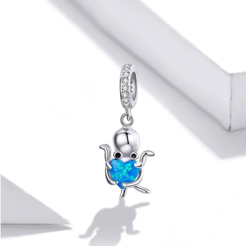 Close-up van een 925 sterling zilveren octopusbedel die een levendige blauwe hartvormige opaal vasthoudt, onderdeel van de oceaan-thema hanger set.