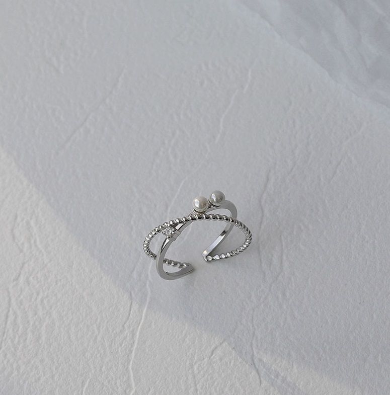 Una toma de estudio en primer plano del anillo cruzado de perla de plata esterlina 925, mostrando su diseño intrincado con dos elegantes perlas y acentos de circonita cúbica brillante.