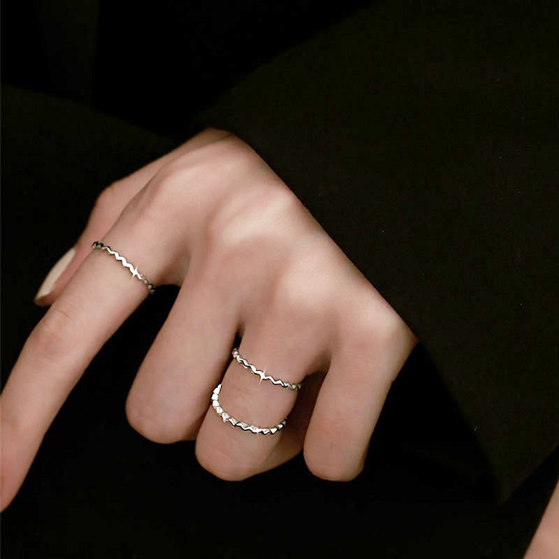 A model's hand showcasing a set of three 925 sterling silver stackable knuckle rings with an elegant waving line design.