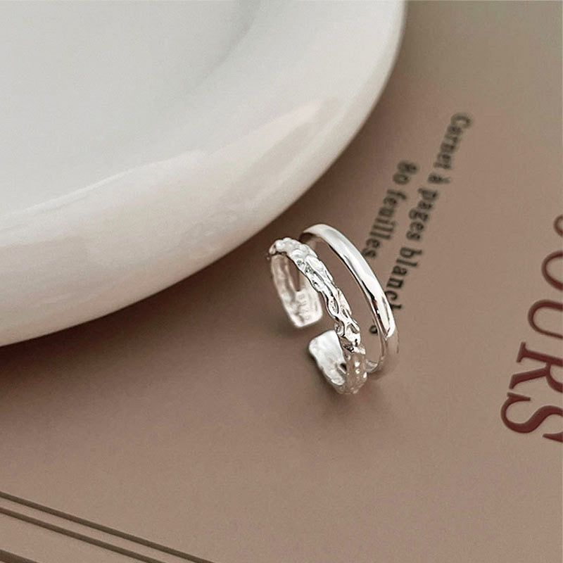 Een set van twee 925 sterling zilveren dual-laags verstelbare ringen met verschillende texturen, elegant weergegeven op een open boek.