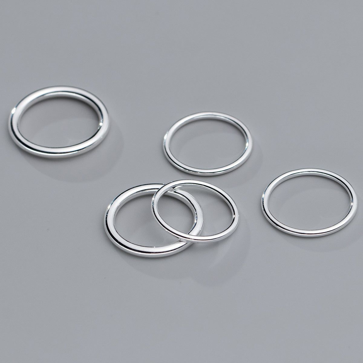 Ein Set aus fünf schlichten stapelbaren Ringen aus 925er Sterlingsilber mit einem schlanken, modernen Design, vor einem neutralen Hintergrund gezeigt.