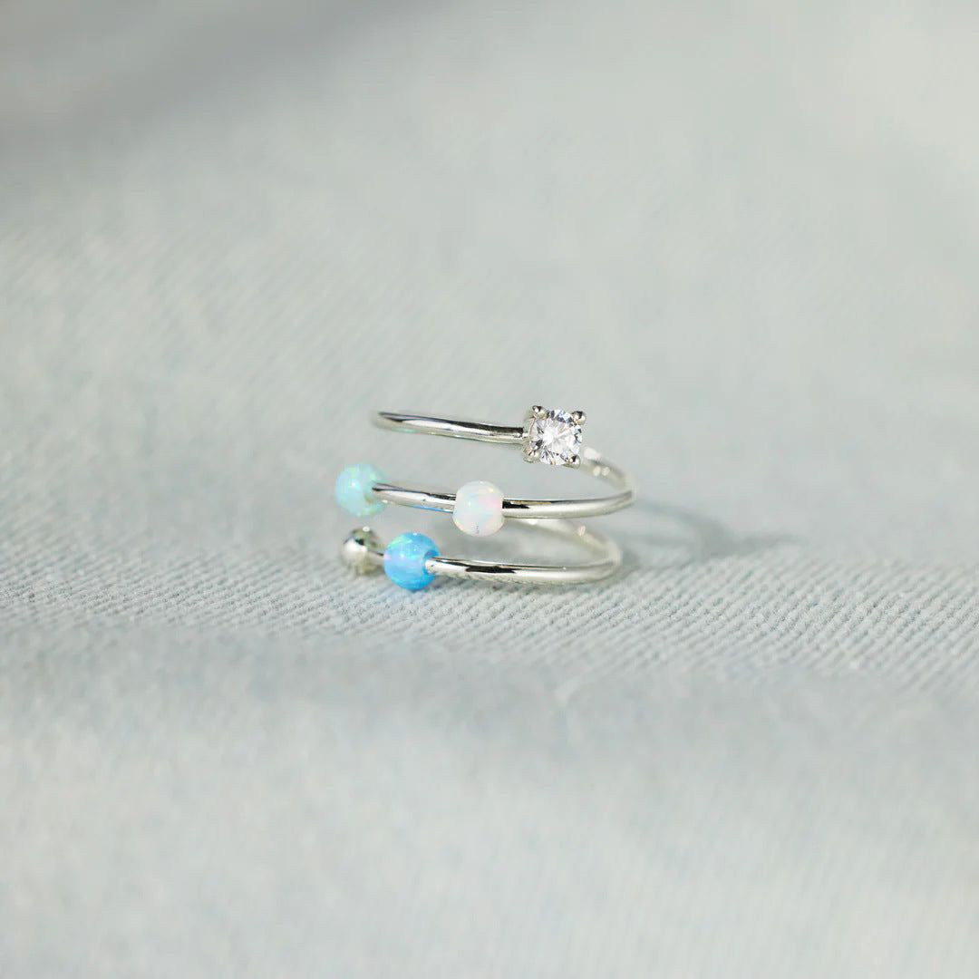Ein Set von Starlit Ocean mehrschichtigen Ringen aus 925er Sterlingsilber, mit einem Triple-Spiral-Design mit Opal- und Zirkonsteinen, auf einem sauberen Hintergrund präsentiert.