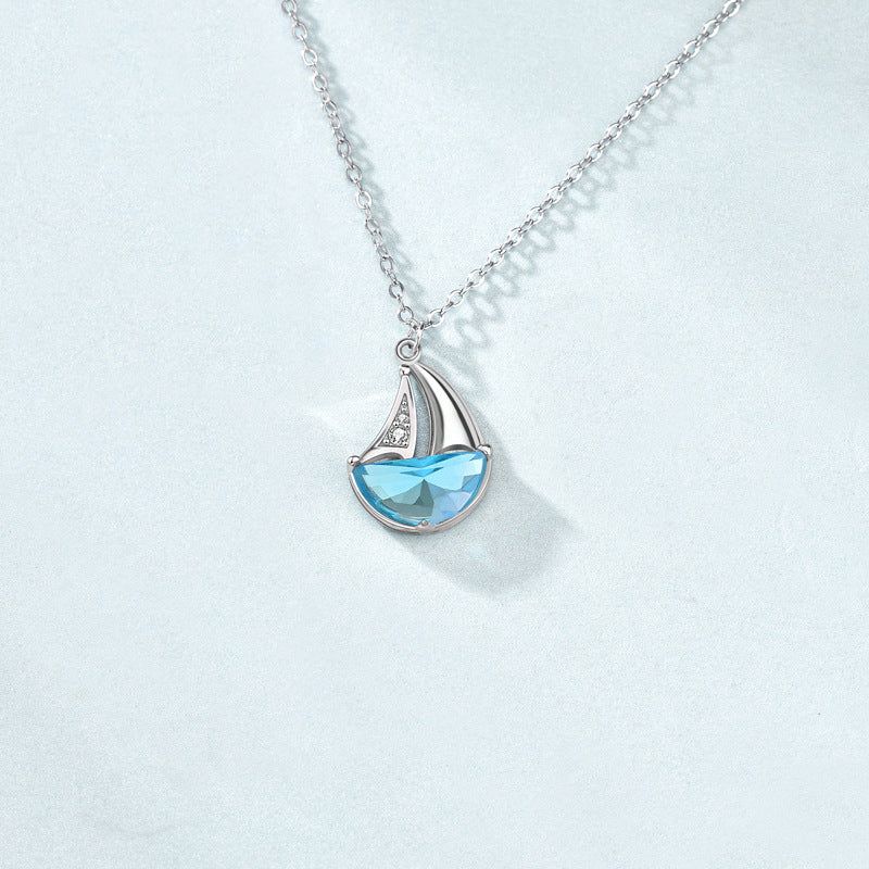 Close-up of a 925 sterling silver sailboat pendant necklace, featuring a light blue CZ gemstone hull and sparkling white CZ stones on the sail.