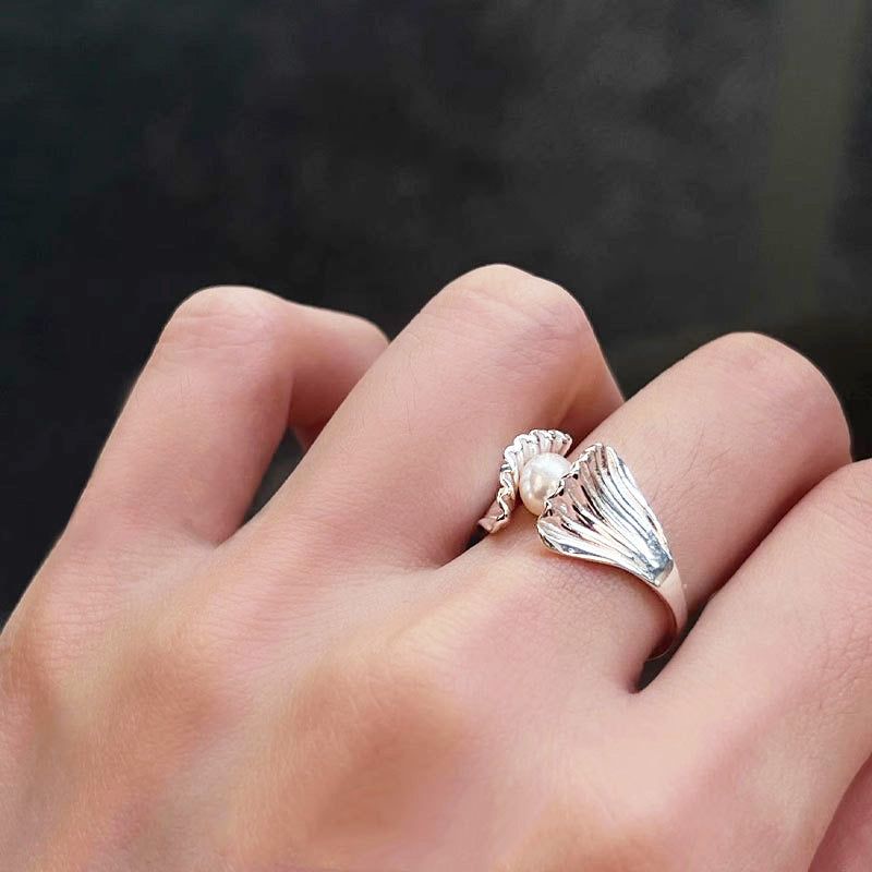 Un anillo ajustable de plata esterlina 925 con un elegante diseño de concha de vieira de estilo francés que sostiene una sola perla lustrosa, usado en un dedo.