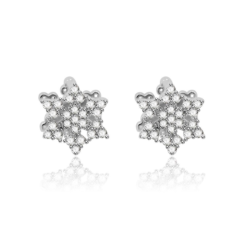 Une paire de boucles d'oreilles Huggie en CZ flocon de neige en argent, avec des charmes flocon de neige ornés de pierres précieuses claires, présentée sur un fond blanc propre.