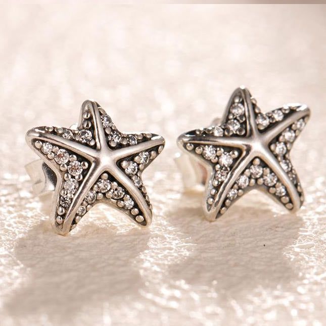 Una vista ravvicinata di un paio di orecchini a perno a forma di stella marina vintage in argento sterling 925, che mostrano i dettagli intricati e le gemme trasparenti scintillanti.