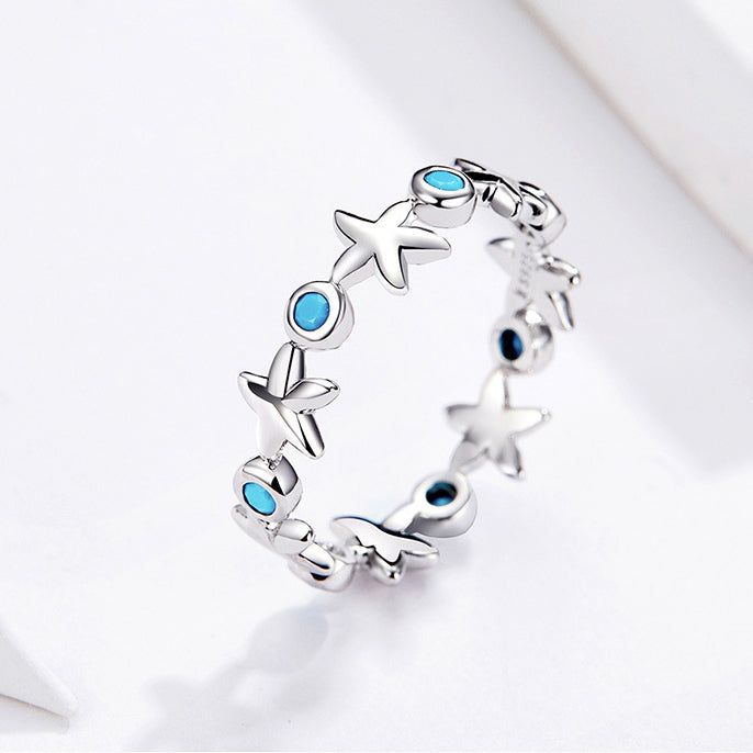 Un conjunto de cinco anillos de plata esterlina 925 con un diseño de estrella de mar inspirado en el océano, adornados con piedras de zirconia azul océano brillantes, exhibidos sobre un fondo neutro.