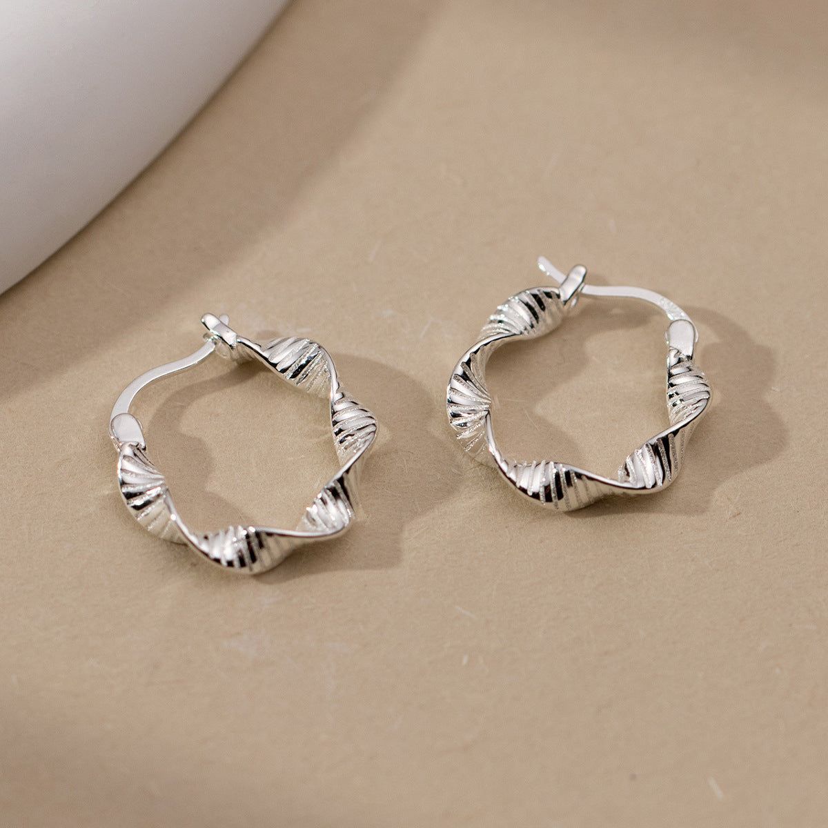 Un paio di orecchini a cerchio in argento sterling 925 con un elegante design geometrico attorcigliato, esposti su uno sfondo neutro.