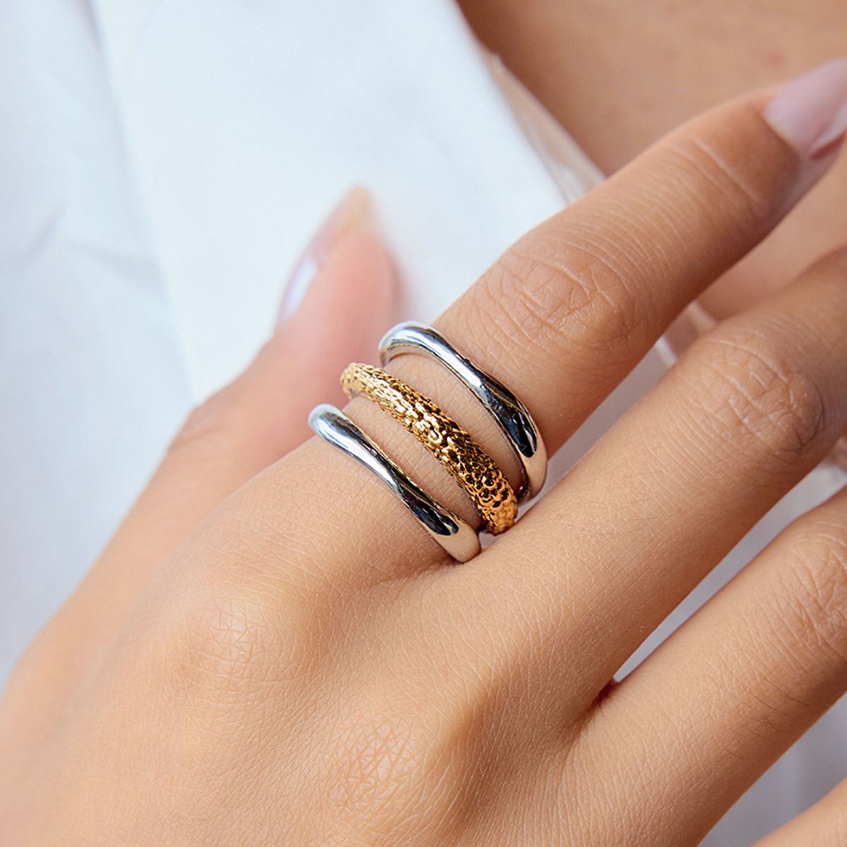 De hand van een model die een stapel minimalistische twee-kleurige (goud en zilver) roestvrijstalen ringen toont, die de trendy stapelbare stijl demonstreert.