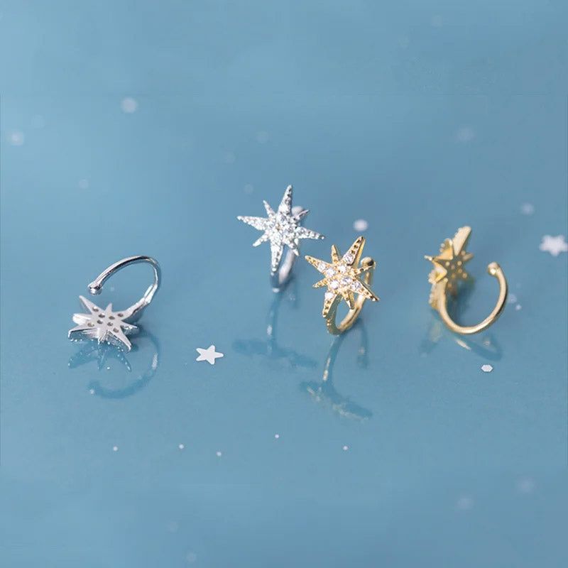 Un set di quattro orecchini a cuffia in argento sterling 925 a forma di stella con pietre di zirconia, esposti in finiture argento e oro su uno sfondo bianco.