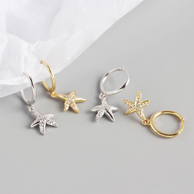 Una foto del prodotto degli orecchini huggie a forma di stella marina in argento sterling 925, che mostrano entrambe le opzioni di colore argento e oro su uno sfondo bianco pulito.