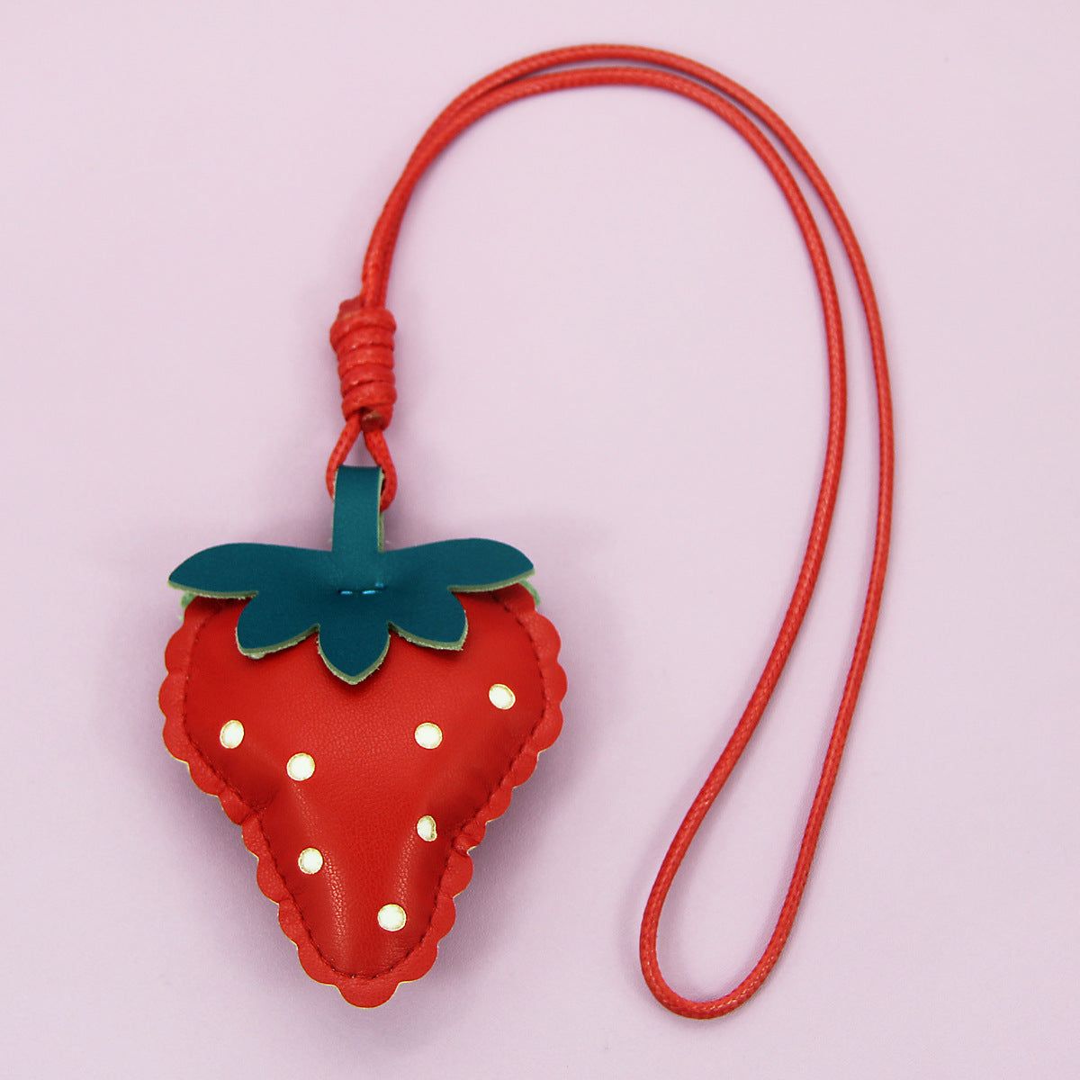 Gros plan sur un porte-clés en cuir PU en forme de fraise, avec des coutures blanches détaillées et un accent de feuille verte, attaché à un cordon rouge.