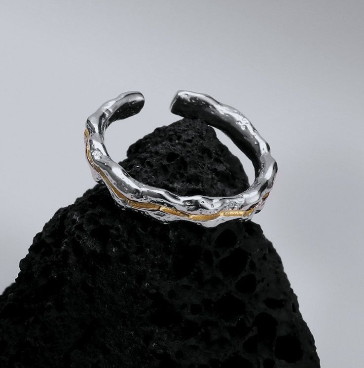 En närbild av 925 sterling silver dubbelpläterad ring, som visar dess unika texturerade yta med eleganta gulddetaljer, vilande på en mörk, naturlig yta.