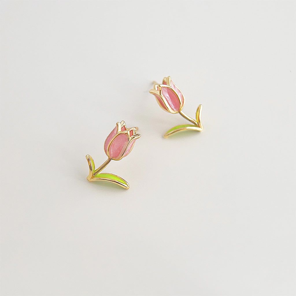 Une paire de boucles d'oreilles en tulipe en émail plaquées or 14k avec des pétales roses délicats et des feuilles vertes, mettant en valeur l'artisanat détaillé.