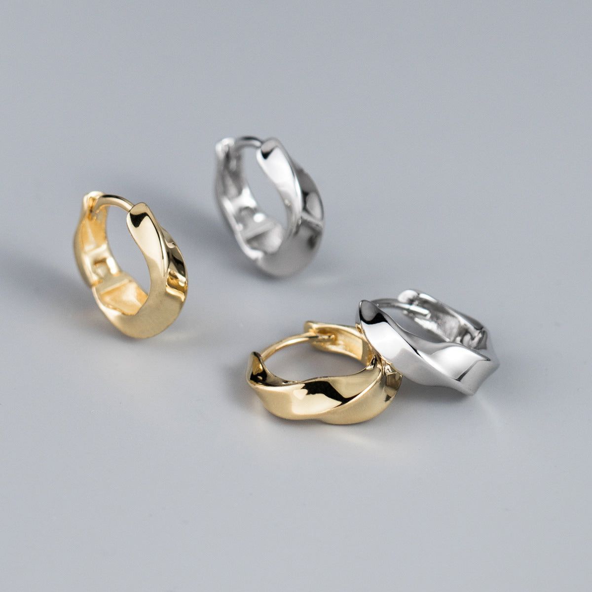 Un set di quattro orecchini a cerchio in argento sterling 925 con design a spirale Mobius, due con finitura argentata lucida e due con finitura dorata, esposti su uno sfondo bianco pulito.