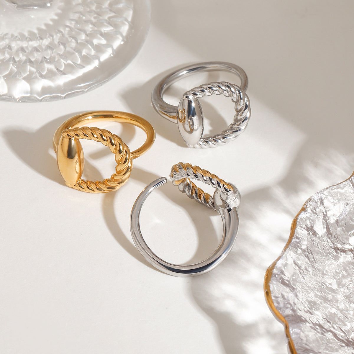 Un set di tre anelli all'ingrosso in acciaio inossidabile con rivestimento PVD in oro 18K e argento, caratterizzati da un elegante design ovale attorcigliato.