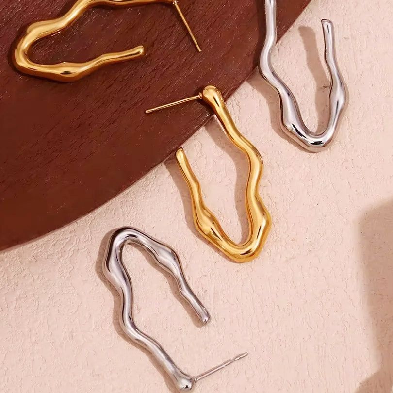 Ein Paar goldene und ein Paar silberne Wellen-V-förmige Creolen aus rostfreiem Stahl, die vor einem neutralen Hintergrund ausgestellt sind.