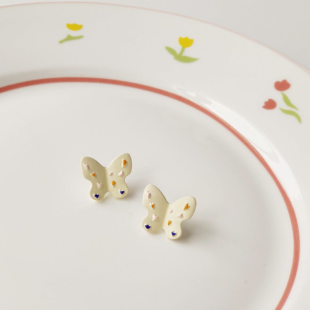 A pair of wholesale white enamel butterfly stud earrings with colorful spots, elegantly displayed on a decorative plate.