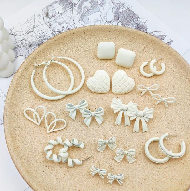 A curated collection of JR Fashion's white enamel earrings, showcasing various styles including hoops and studs, elegantly displayed on a beige plate.