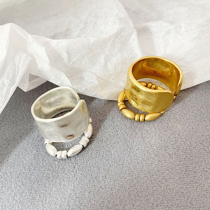 Un par de anillos abiertos de dos capas de estilo francés en acabados de oro y plata, con elegante detalle de cuentas sobre un fondo blanco.