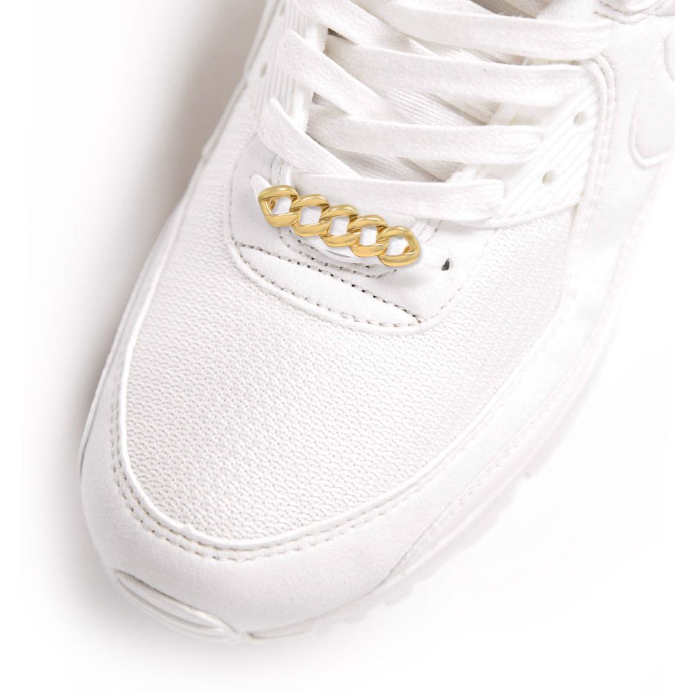 Un primo piano di una sneaker bianca con un elegante ciondolo a catena cubana dorata attaccato ai lacci.